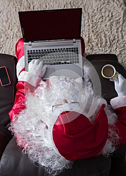 Overhead of Santa Claus relaxing in sofa at home. Using laptop f