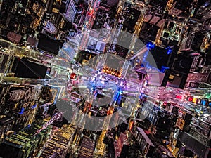 Overhead shot of buildings and streets around Times Square. Advertisements and displays glowing colourful light