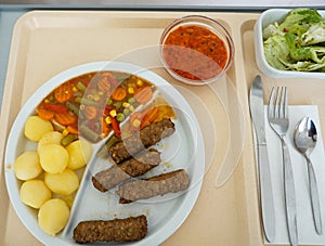 An overhead shot of Cevapcici with potatoes and vegetables on a partitioned plate
