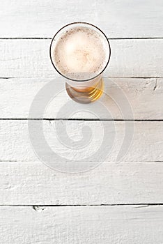 Overhead shot of cold beer glass on white wooden background with copyspace