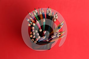 Overhead shot of colorful pencils in a metal pen holder on a red background