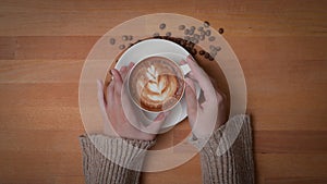 Overhead shot of female hands holding a cup of latte coffee on wooden