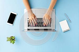 Overhead shot of female hands using laptop on blue office desktop. Business background.