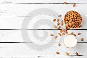 Overhead shot of glass of almond milk on white wooden background with almonds in bowl and copyspace