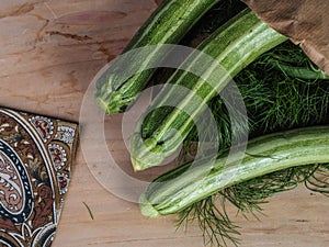 Overhead shot of a group of  isolated three green biologic zucchini veggies fruit over a light brown table and a paper recycled