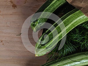 Overhead shot of a group of  isolated three green biologic zucchini veggies fruit over a light brown table and a paper recycled