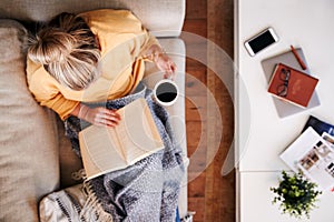 Overhead Shot Looking Down On Woman At Home Lying On Reading Book And Drinking Coffee