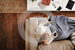 Overhead Shot Looking Down On Woman At Home Lying On Sofa Watching Television