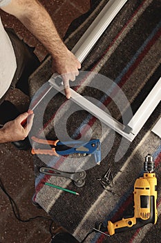 Overhead shot of man assembling a Modena window frame. He uses a screwdriver. On the table you can see working tools: screwdriver