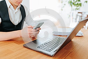 An overhead shot of a man's hands typing on a laptop keyboard and holding a smartphon