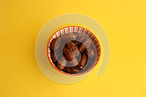 Overhead shot of Medjool dates on in a decorative bowl on a yellow table