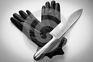 Overhead shot of a metal knife over black gloves on a  white surface