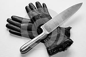 Overhead shot of a metal knife over black gloves on a  white surface