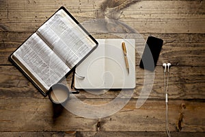 Overhead shot of a notebook with a fountain pen near an open book and smartphone on wooden table