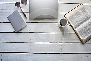 Overhead shot of an open bible near a coffee and, laptob, notepad with a pen