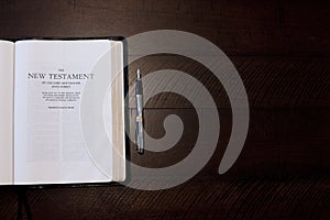 Overhead shot of an open bible near a pen on a wooden surface