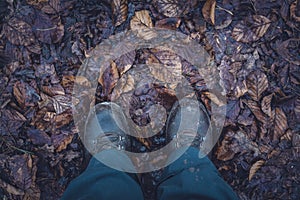 Overhead shot of a person`s feet with boots standing in a muddy ground with wet leaves