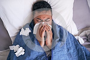 An overhead shot of a sick man blowing his nose while lying in bed