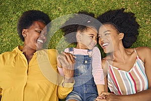 Overhead Shot Of Smiling Multi-Generation Female Family Lying On Grass In Garden Together