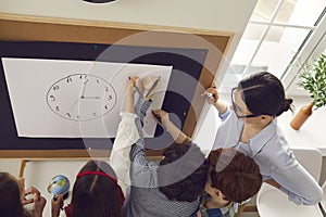 Overhead shot of teacher teaching pupil clock time standing next to blackboard