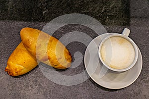 Overhead shot of two pies and a cappuccino in a white cup on a gray table