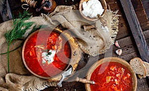 Overhead shot of two wooden bowls with tasty Ukrainian or Russian traditional beetroot soup borscht with sour cream