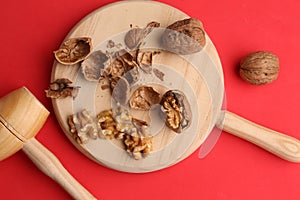 Overhead shot of walnuts on a wooden cutting board with a small hammer isolated on a red background