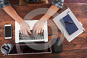 Overhead shot of white mans hands typing on a laptop