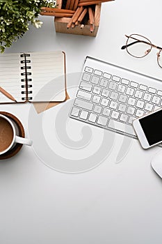 White office desk with smart phone, notebook, coffee cup, glasses and keyboard.