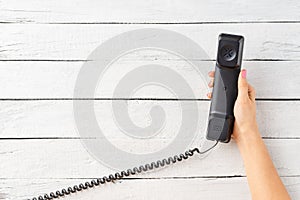 Overhead shot of womanâ€™s hand holding retro phone on rustic wooden background with copyspace.