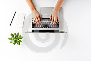 Overhead shot of womanâ€™s hands working on laptop on white table with accessories. Office desktop.