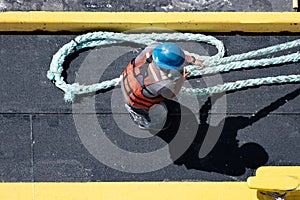 Maritime Work Ethic: Overhead Shot of a Worker in Reflective Vest and Blue Helmet Pulling a Thick Rope on a Ship