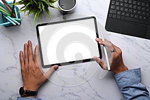 Overhead shot of young man graphic designer holding stylus pen and digital tablet with blank screen on marble desk.