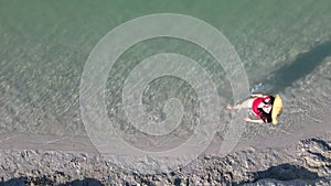 overhead top view of woman in red swimsuit walking by sandy beach