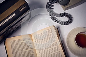 Overhead view of book with tea and telephone by radio