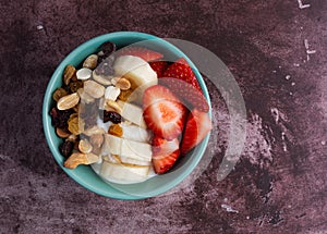 Overhead view of a bowl with plain Greek yogurt candy trail mix bananas and strawberries on a marron tabletop illuminated with