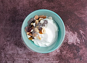 Overhead view of a bowl with plain Greek yogurt and a candy trail mix on a marron tabletop illuminated with natural light