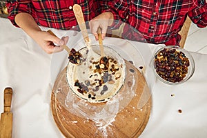 Overhead view of children`s hands sprinkling ready-made dough in bowl with dried fruits and nuts, preparing dough for Christmas