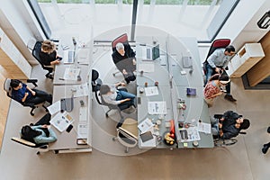 Overhead view of a collaborative workspace with a group of people engaged in discussion, working on computers and