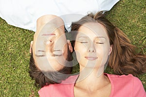 Overhead View Of Couple Lying On Grass With Eyes Closed