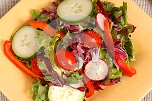 An overhead view of a crisp healthy salad on a yellow plate