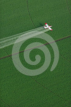 An overhead view of a crop duster spraying green farmland