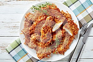 Overhead view of delicious grated potato coated and deep fried pork chops on a plate on a rustic white wooden table with napkin,