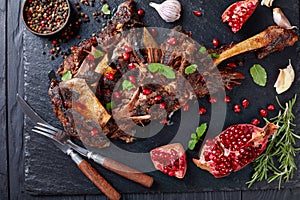 Overhead view of delicious roast leg of lamb served with pomegranate seeds, mint leaves, spices and rosemary on a black slate