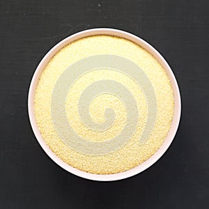 Overhead view, dry semolina durum flour in a pink bowl over black background, top view. Overhead, from above, flat lay. Close-up