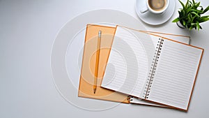 Empty notebook, coffee cup, house plant and copy space on white table.