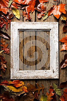 Overhead view of empty old picture frame with autumn leaves over wooden table