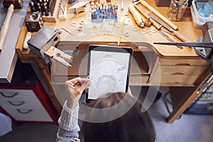 Overhead View Of Female Jeweller Comparing Ring With Drawn Design On Digital Tablet In Studio