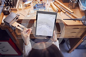 Overhead View Of Female Jeweller Comparing Ring With Drawn Design On Digital Tablet In Studio