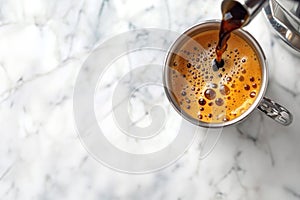 Overhead view of fresh black coffee being poured into white mug on marble tabletop